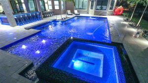 Modern luxury pool with glowing spa, sleek water features, and vibrant LED lighting.